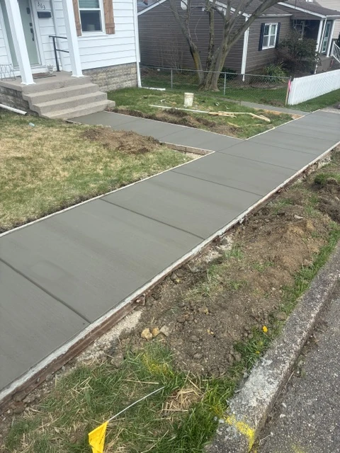 Newly finished concrete sidewalk running alongside a residential yard